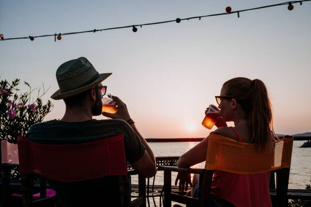 Young couple enjoying beer and sunset in a beach bar Young couple enjoying beer and sunset in a beach bar beach bar stock pictures, royalty-free photos & images