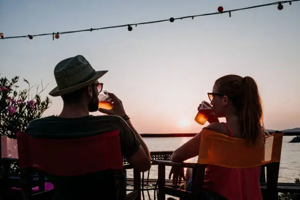 Photo of Young couple enjoying beer and sunset in a beach bar