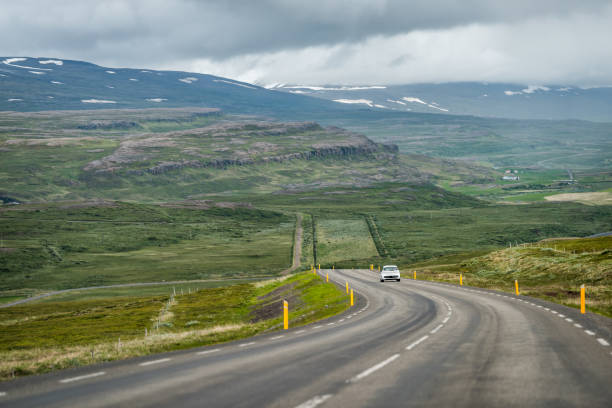 Photo of Ring road in east Iceland highlands highway with barren bare green landscape and car on steep slope with overcast cloudy stormy weather near Egilsstadir
