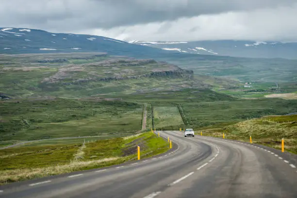 Ring road in east Iceland highlands highway with barren bare green landscape and car on steep slope with overcast cloudy stormy weather near Egilsstadir