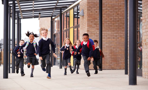 Primary school kids, wearing school uniforms and backpacks, running on a walkway outside their school building, front view Primary school kids, wearing school uniforms and backpacks, running on a walkway outside their school building, front view primary school stock pictures, royalty-free photos & images