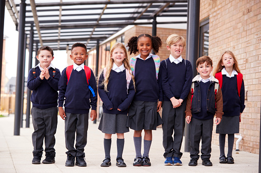 La escuela primaria los niños de pie en una fila en una calzada fuera de la escuela, sonriendo a la cámara, bajo ángulo photo