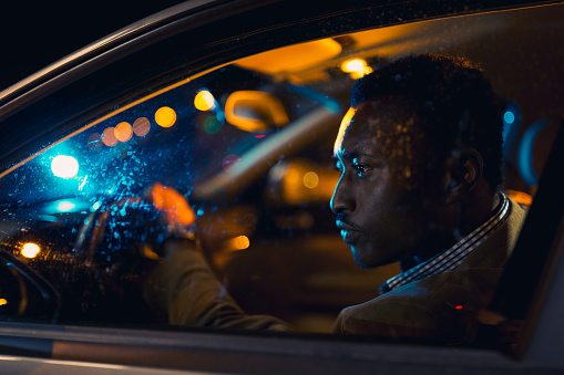 Handsome businessman, on a business trip, driving at night. African ethnicity