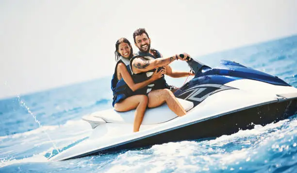 Young couple jet skiing on a open sea. They are smiling and looking at camera.