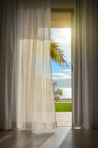 Photo of curtain in wind with view to palms and beach