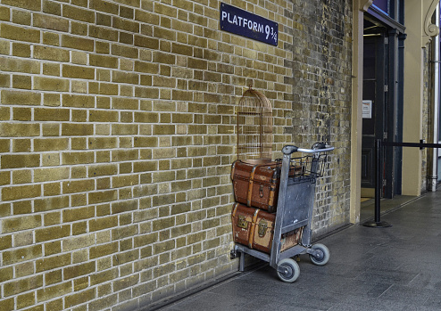 London, United Kingdom, June 2018. Platform 9 and 3/4 at Kings Cross Station, London. A trolly stuck in the wall where fans emulate the Harry Potter adventures. A service assistant for the photo.