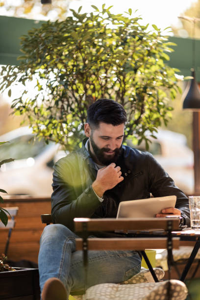 istock Young man outside a coffee shop looking at his tablet 1092228802