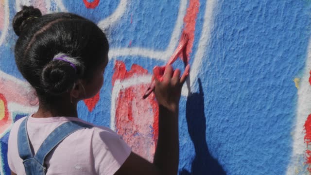 Girl painting mural on sunny wall