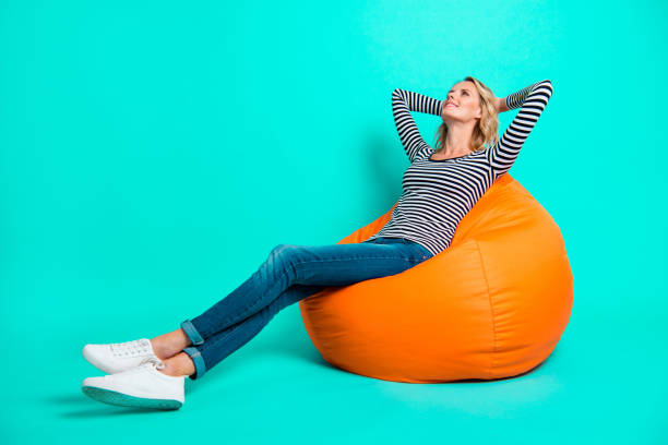 Profile side view full length body size nice pretty charming attractive cheerful wavy-haired girl in striped pullover jeans denim sitting resting after work day isolated on shine turquoise background