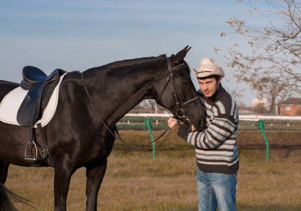 istock Man nearby horse, striped pullover, blue jeans, hat, close up 1092259268
