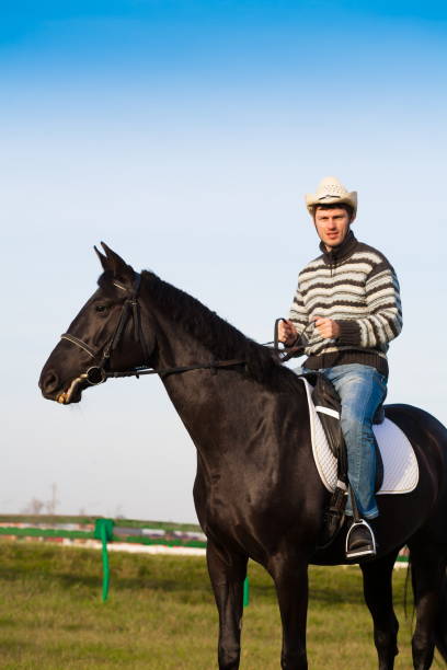 istock Man riding horse, striped pullover, blue jeans, hat, close up 1092260034