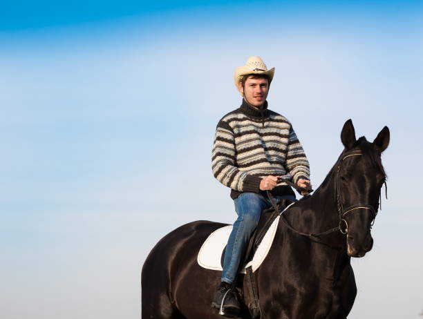 istock Man riding horse, striped pullover, blue jeans, hat, close up 1092260104