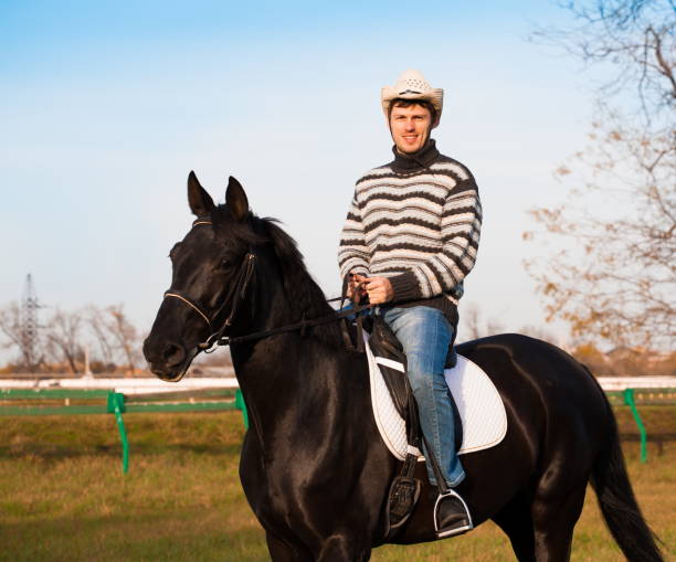 istock Man riding horse, striped pullover, blue jeans, hat, close up 1092261460