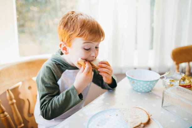 Young Boy Eating a Sandwich Two children making their sandwiches for lunch. making a sandwich stock pictures, royalty-free photos & images