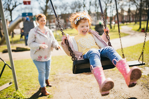 Little girl being pushed on a swing set by her Mother.