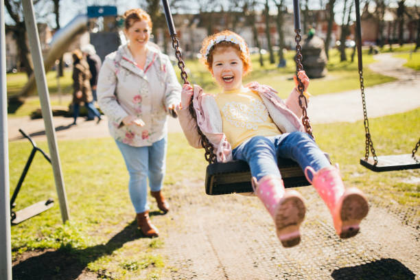 Fun in the Park with Mum Little girl being pushed on a swing set by her Mother. swing play equipment photos stock pictures, royalty-free photos & images