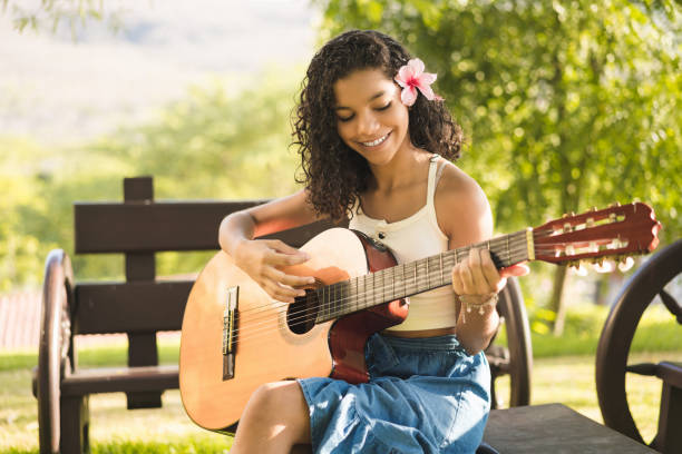 full-length portrait of a young Latina woman sitting with a guitar between her legs.