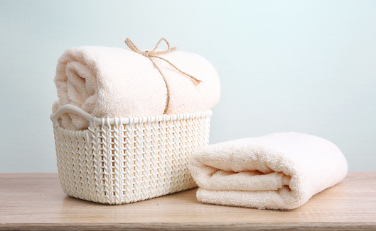 Fresh clean towel in bascket, towels stack on wooden table empty copy space background.