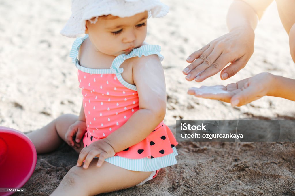 Happy laughing toddler girl having fun on sand Suntan Lotion Stock Photo