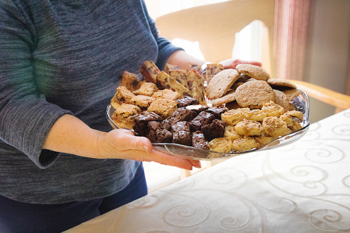 Female bringing dessert platter to the table. Included are fruit cake, squares, brownies, cookies and sugar swirls.