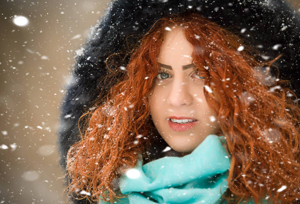 Beautiful girl with red curly hair, posing as snow falls