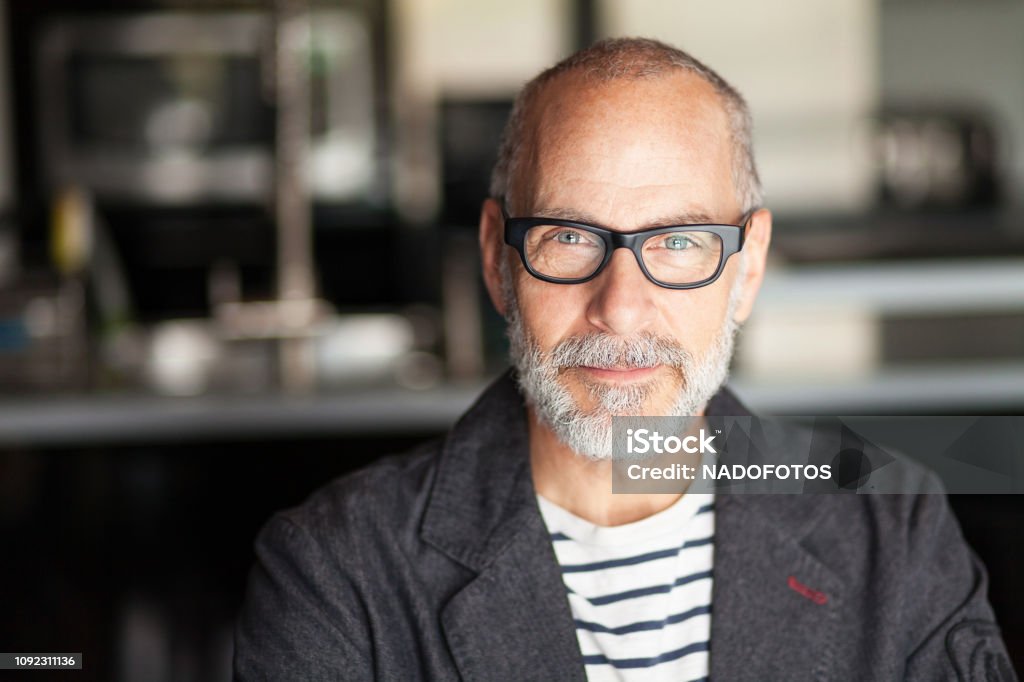 Portrait Of A Senior Man Looking At The Camera. He's confident Portrait Of A Senior Man Looking At The Camera. He's confident. He's working at home. Kitchen background. He's wearing eyeglasses Portrait Stock Photo