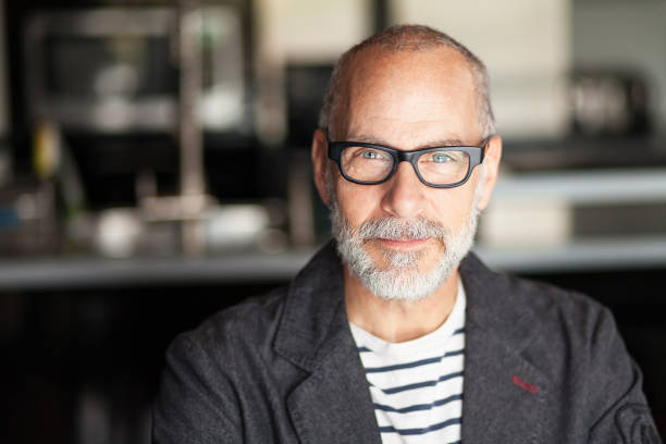 Portrait Of A Senior Man Looking At The Camera. He's confident Portrait Of A Senior Man Looking At The Camera. He's confident. He's working at home. Kitchen background. He's wearing eyeglasses smirking stock pictures, royalty-free photos & images