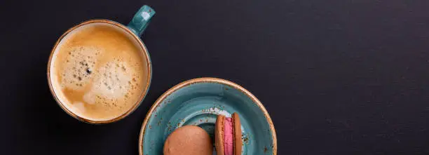 Photo of Blue cup of coffee and macaroons on the dark wooden table. Coffe break. Top view. Flat lay