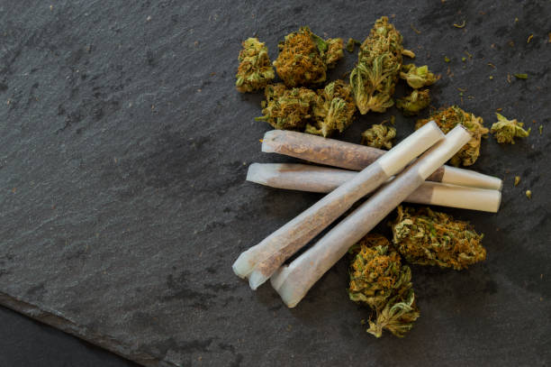 joints de marijuana prêt à fumée et un tas de mauvaises herbes bourgeons sur la table en pierre noire. bouchent arrière-plan avec des détails de la drogue. copiez l’espace gauche. - drug dealer photos photos et images de collection