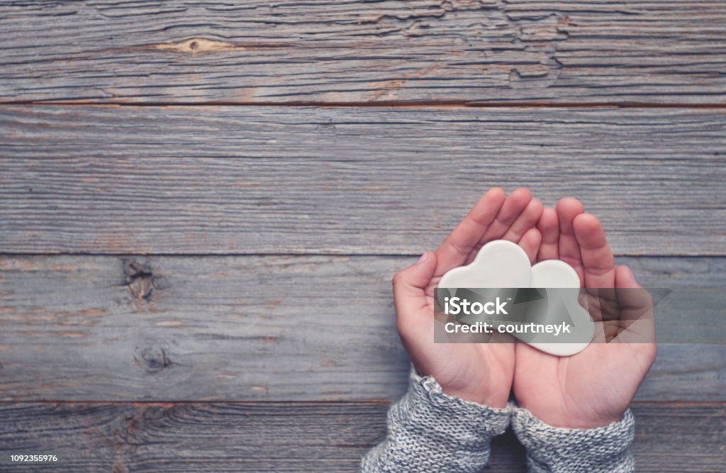 Woman holding two white love hearts. Woman holding two white love hearts. A woman is holding them in her hands. There is a rustic wood table underneath her hands. Valentines day or anniversary concept. Copy space. Repetition Stock Photo