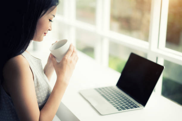 istock Asian beautiful young smiling woman working on laptop and drinking coffee while sitting in cafe or coffee shop. 1092361046