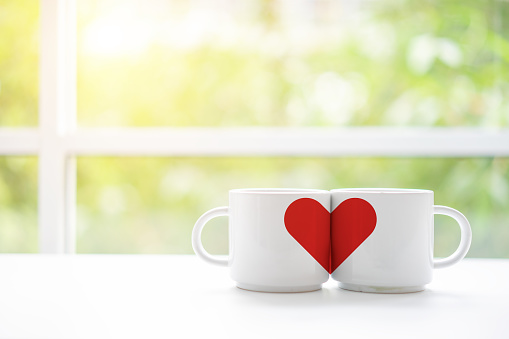 Mugs cups of coffee or tea for two lovers honeymoon wedding morning in coffee shop with green nature in background. Copy space with white wooden table. Valentines day concept.