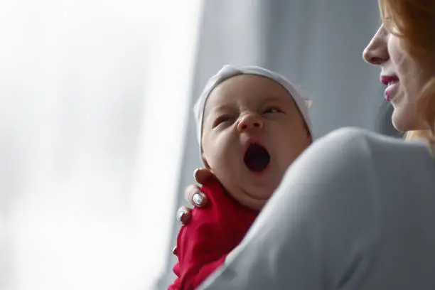 Photo of Mother holding cute newborn baby girl in her arms. Sleepy baby yawning.