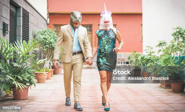 Crazy Senior Couple Wearing Dinosaur And Unicorn Mask Mature Trendy People Having Fun Masked At Carnival Parade Absurd Eccentric Surreal Fest And Funny Masquerade Concept Stock Photo - Download Image Now