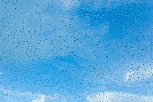 Raindrops on the windshield; in the background blue sky and white clouds, California
