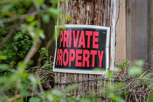 closeup of a private property sign stapled to barbed wire post with thorns