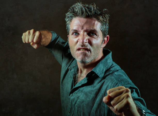young upset and aggressive man in pub raising fist threatening throwing punch ready to fight as the violent thug troublemaker and furious wasted guy isolated on dark background stock photo
