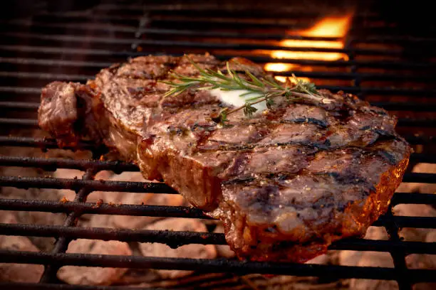 Photo of Large Juicy Beef Rib Eye Steak on a Hot Grill with Charcoal and Flames