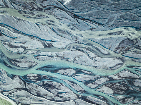 A drone aerial shot from above of a green blue silver looking glacier stream in iceland with interesting patterns as a background