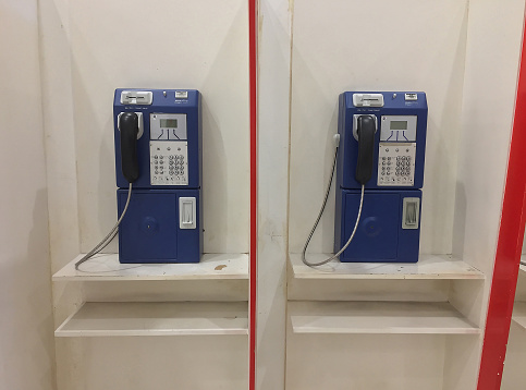Two blue public telephones on white counter (rarely used nowaday)