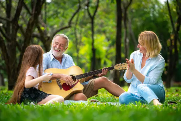 Photo of Happy family play guitar and sing together in park