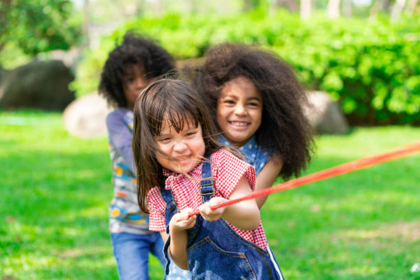 happy children playing tug of war in the park. - tug o war imagens e fotografias de stock