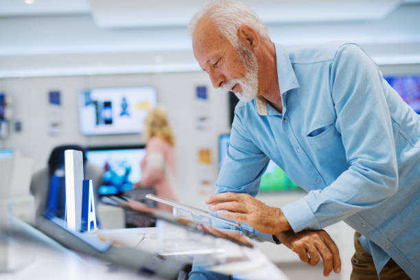 istock Senior man with serious face testing tablet he want to buy and leaning on the stand while standing in tech store. 1092525248
