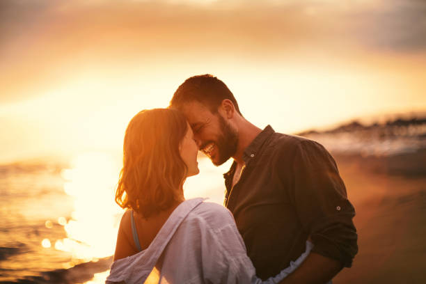 Summer romance. Young couple looking each other on the beach at late sunset. Love is in the air. They are about to kiss. flirty stock pictures, royalty-free photos & images