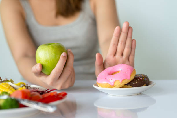 dieta lub dobra koncepcja zdrowia. młoda kobieta odrzuca fast foody lub niezdrowe jedzenie, takie jak pączek lub deser, i wybiera zdrową żywność, taką jak świeże owoce lub warzywa. - carbohydrate zdjęcia i obrazy z banku zdjęć