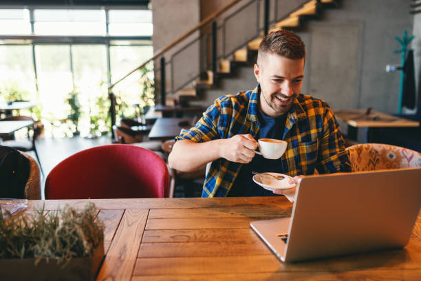 istock Freelancer with smile on his face drinking coffee and looking at laptop while sitting in cafeteria. 1092549986