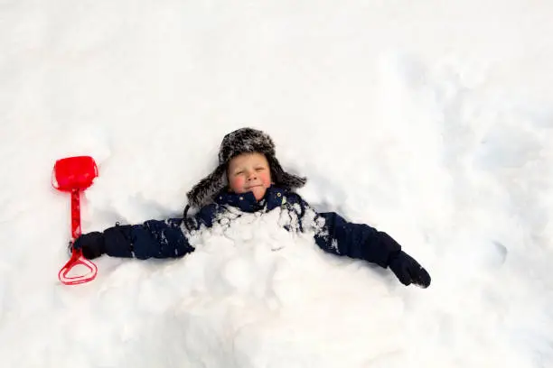 Winter day, a lot of snow, the child buried himself with a children's shovel around the neck in the snow.