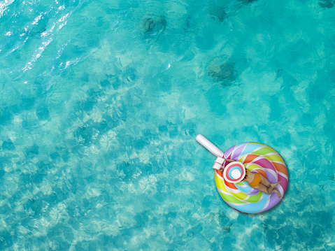 Aerial top view of woman bikini enjoy with reading a book, playing, laying in inflatable swimming tube in the sea water, enjoy feel comfortable in long holidays vacation in summertime at the sea\