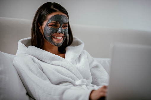 Young girl with purifying black face mask using computer. Shadow DOF. Developed from RAW; retouched with special care and attention; Small amount of grain added for best final impression. 16 bit Adobe RGB color profile.