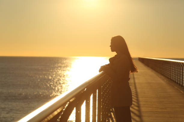 mulher sozinha, contemplando o mar ao pôr do sol - looking at view searching looking sea - fotografias e filmes do acervo